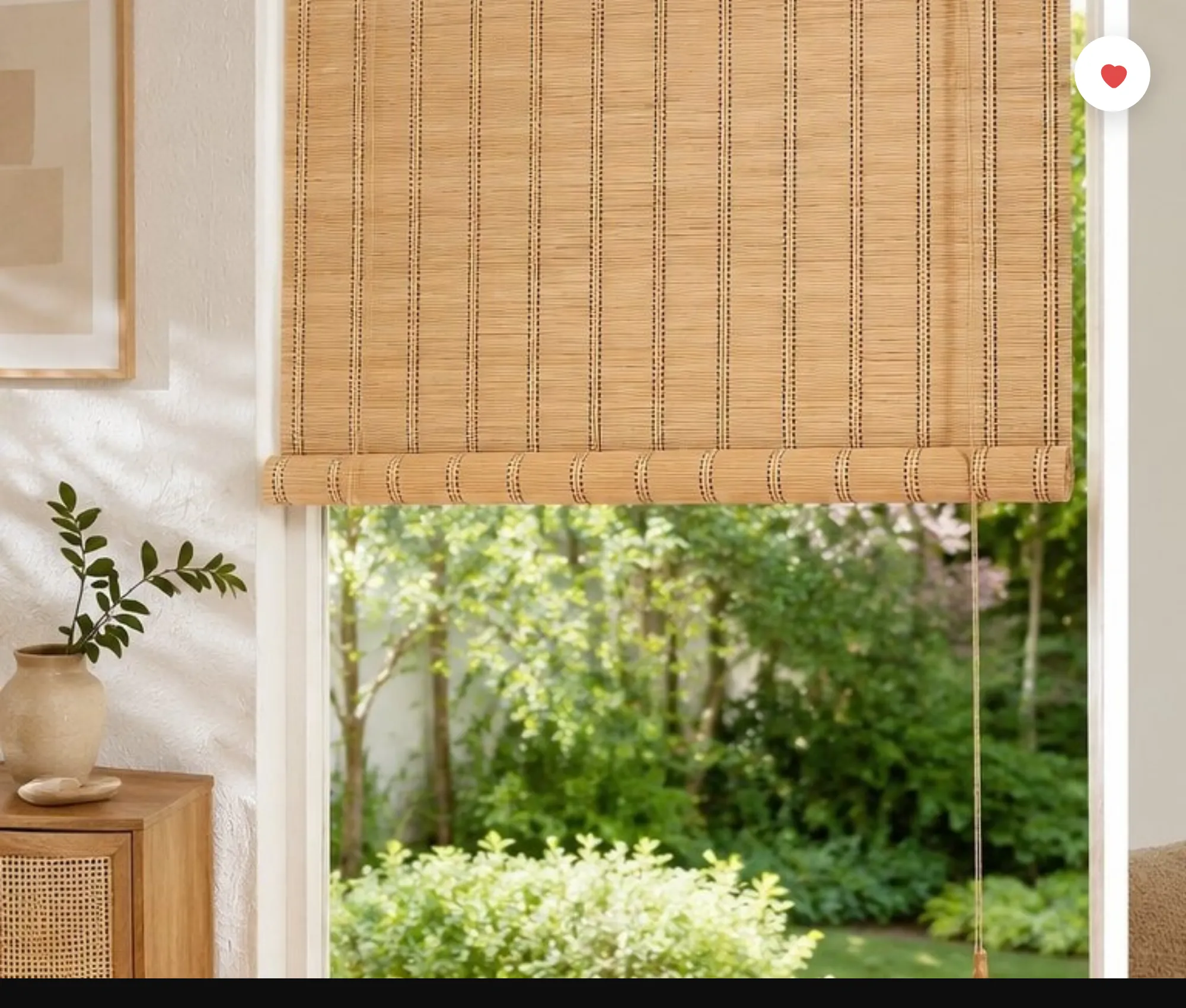 Natural bamboo chick blinds half-rolled over a tall window with a garden view, in a soft modern Indian living room with cane cabinet and plants.