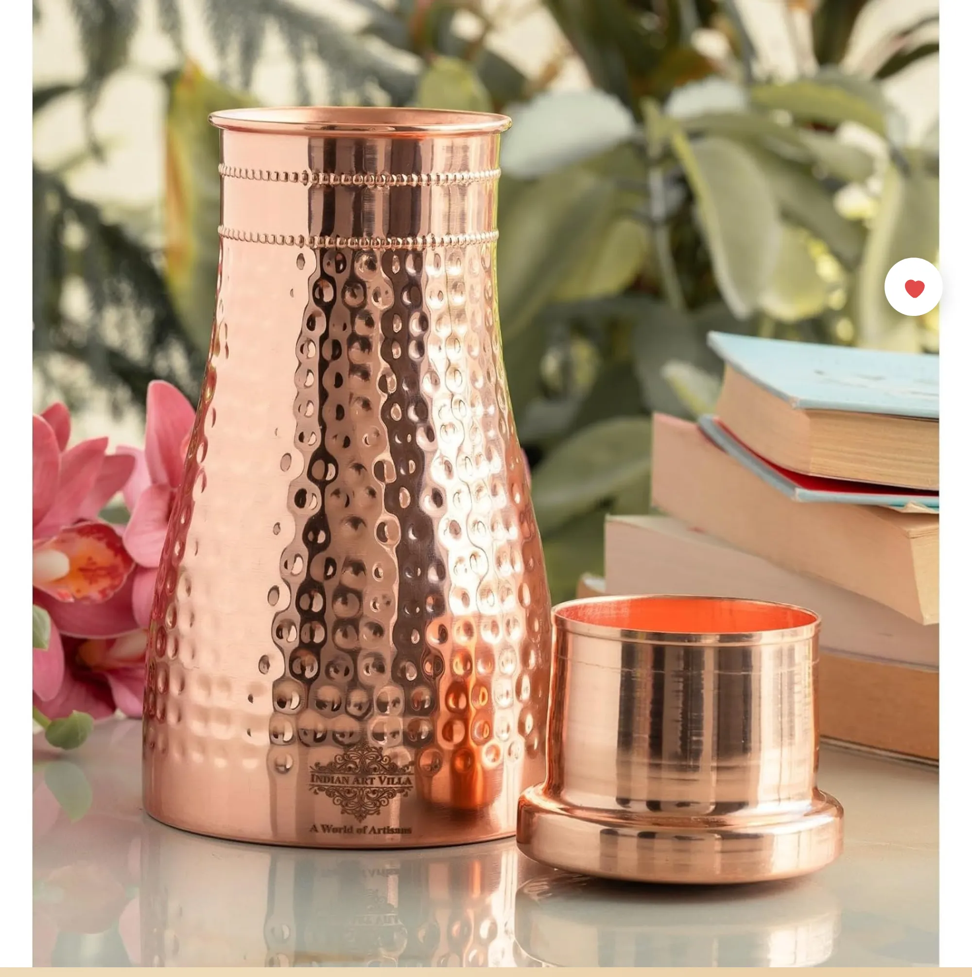 Hammered copper water bottle with cup-style lid on a bedside table next to a lotus flower and a stack of books.