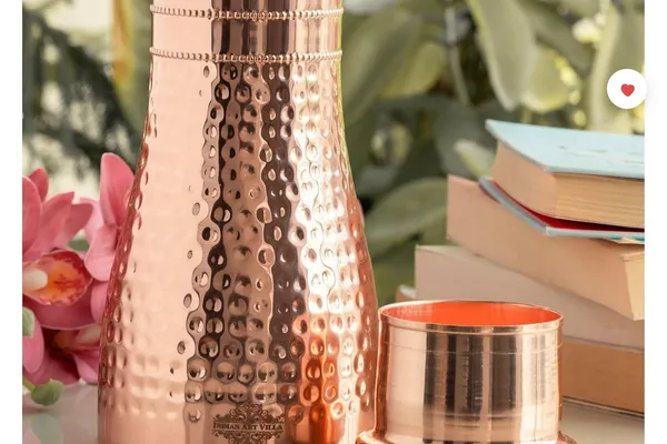 Hammered copper water bottle with cup-style lid on a bedside table next to a lotus flower and a stack of books.